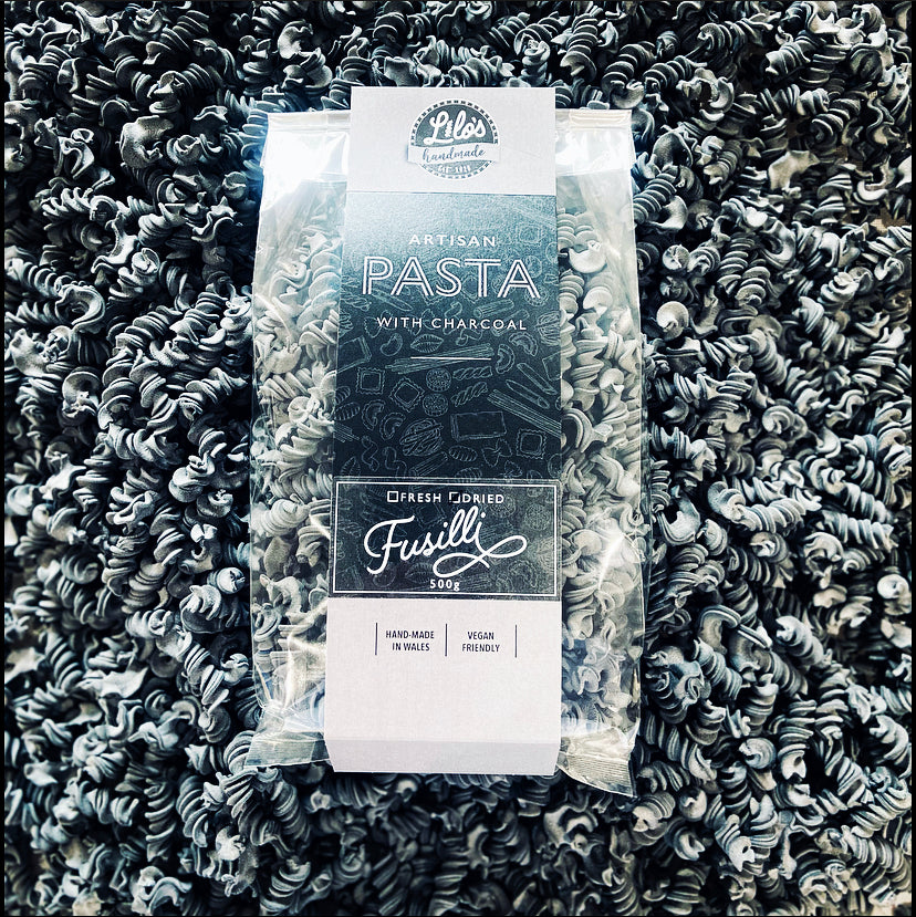 Packaged fusilli pasta with charcoal flavor on a bed of black fusilli pasta.