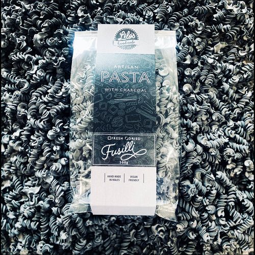 Packaged fusilli pasta with charcoal flavor on a bed of black fusilli pasta.