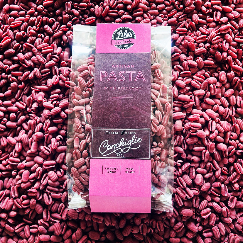 Packaged pink pasta with a purple label on a bed of pink pasta.