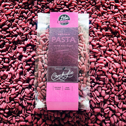 Packaged pink pasta with a purple label on a bed of pink pasta.