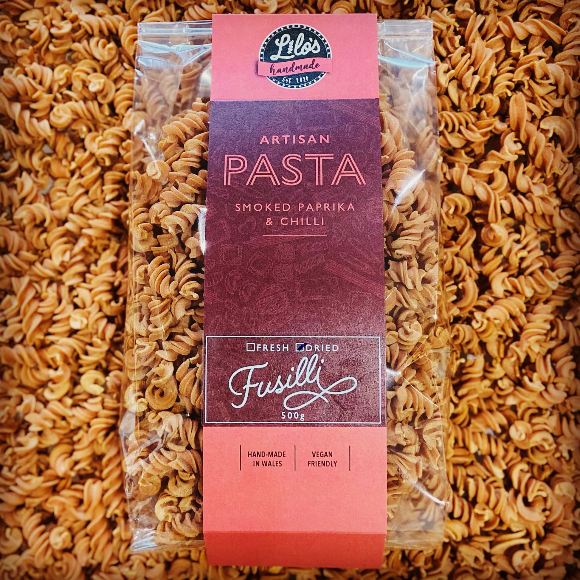 Packaged fusilli pasta with an orange label on a bed of fusilli pasta.