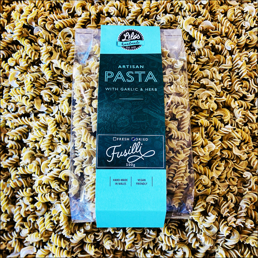 Packaged artisan pasta with garlic and herb flavor on a bed of fusilli pasta.
